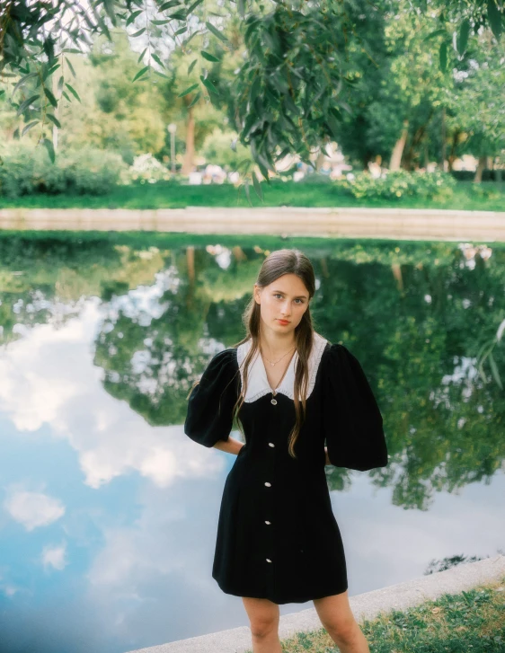 girl poses with her dress off, against a tree filled lake