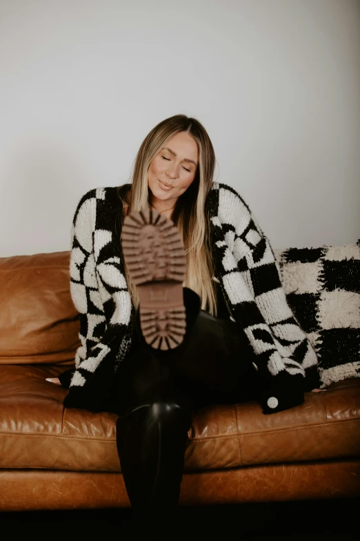 a smiling woman wearing leather legging sitting on a brown couch