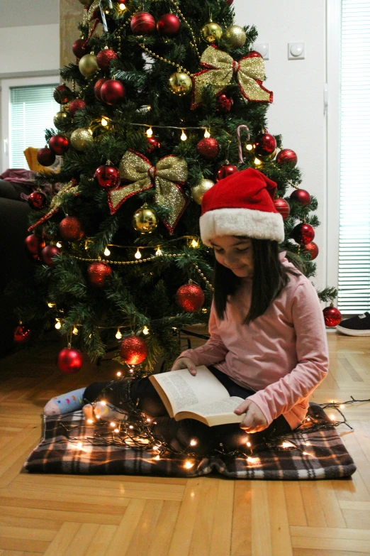 a girl reads a book by a christmas tree