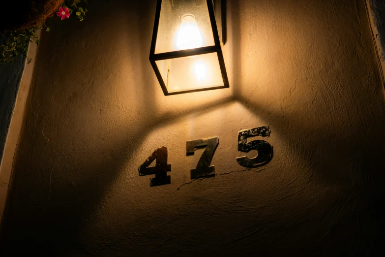 a lit light shines on the side of a house number sign