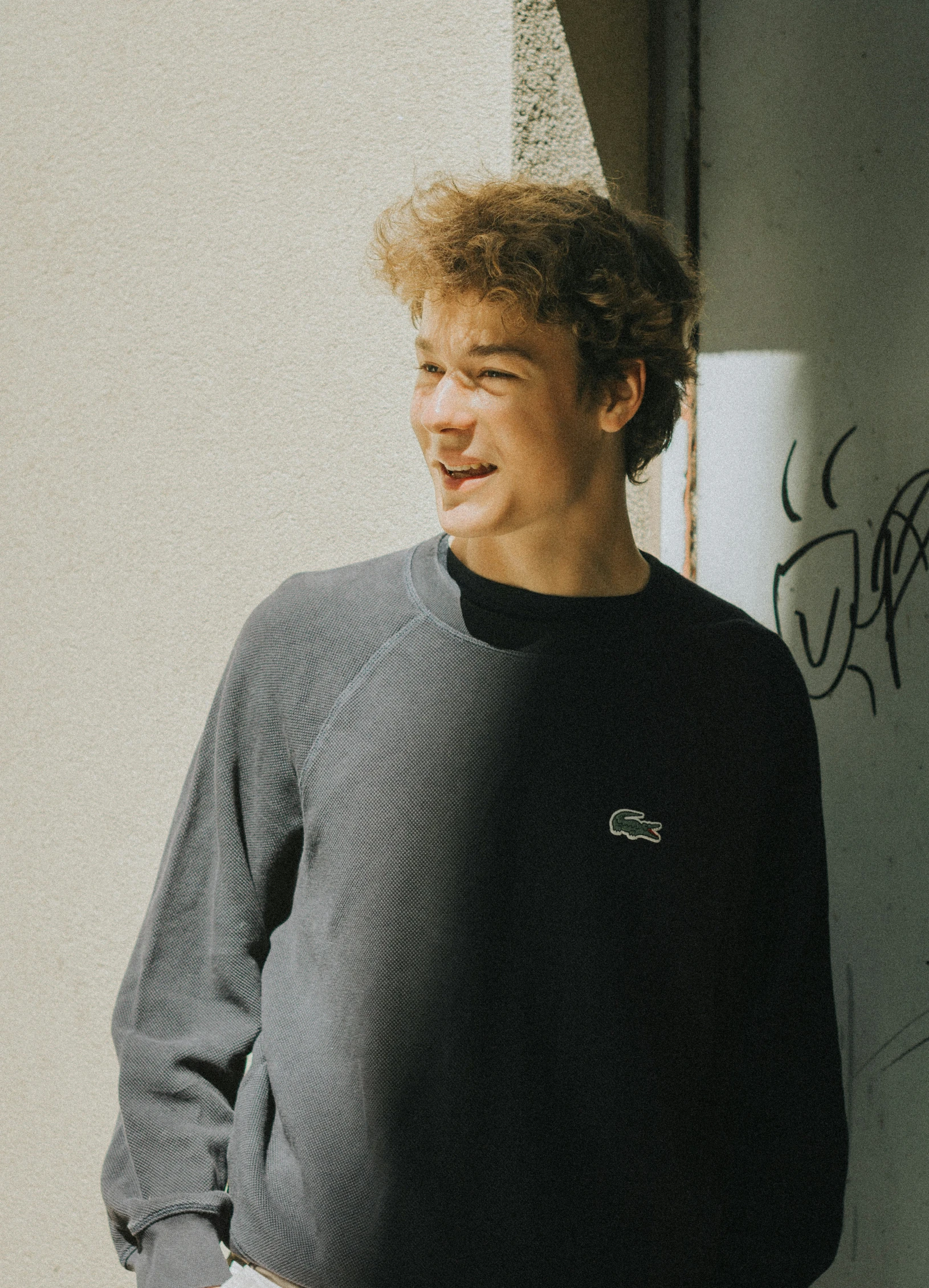 a man in a gray sweater leaning against a wall