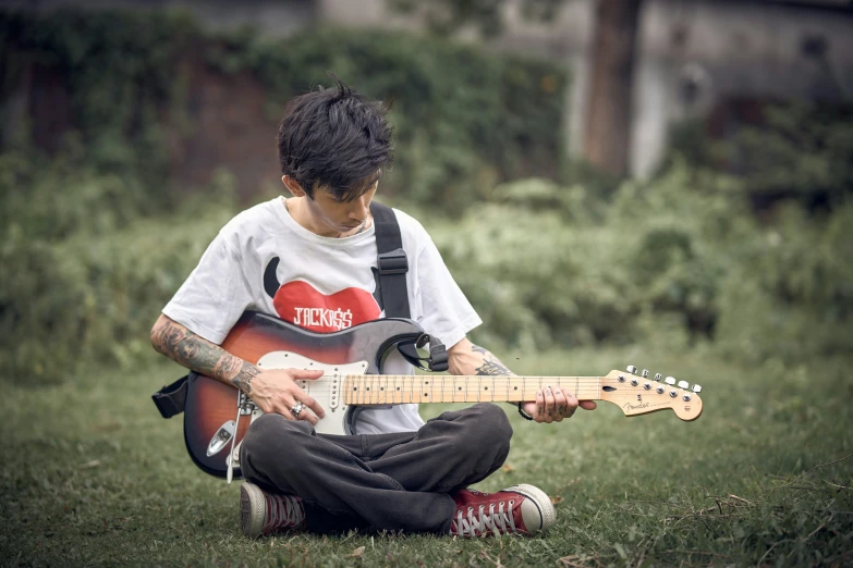 a young man is sitting in the grass playing an electric guitar