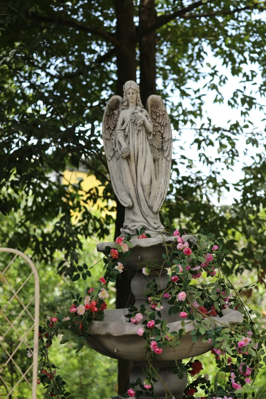 an angel statue with pink flowers around it