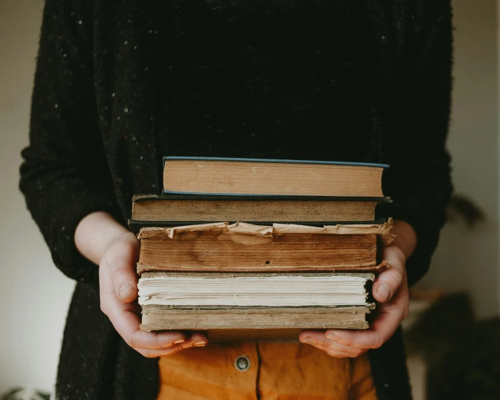 woman in black jacket holding a stack of books