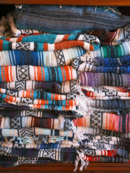 a pile of brightly colored blankets sits on a wooden surface