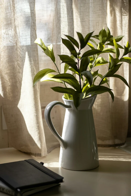 green plants sit in a white vase next to a notebook