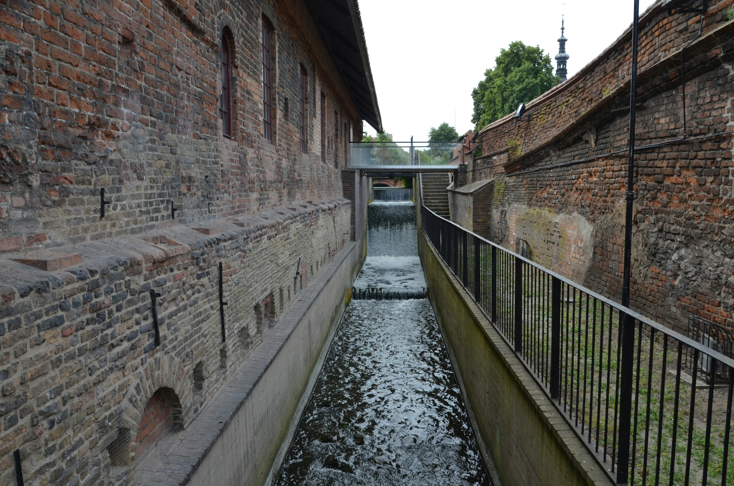 a narrow brick walkway with water running between the two buildings