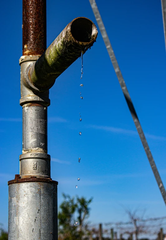 a very long metal pipe with a water drop coming from it