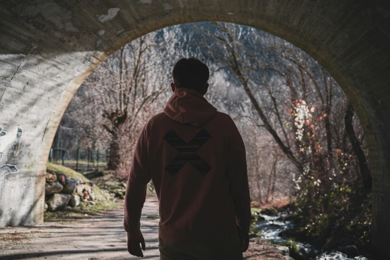 man walking through an overpass and towards the forest