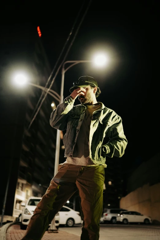 man in the city with green jacket and black hat talking on his cellphone at night