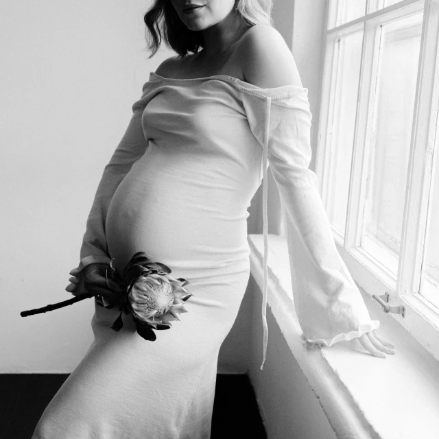 a pregnant woman standing next to a window looking in