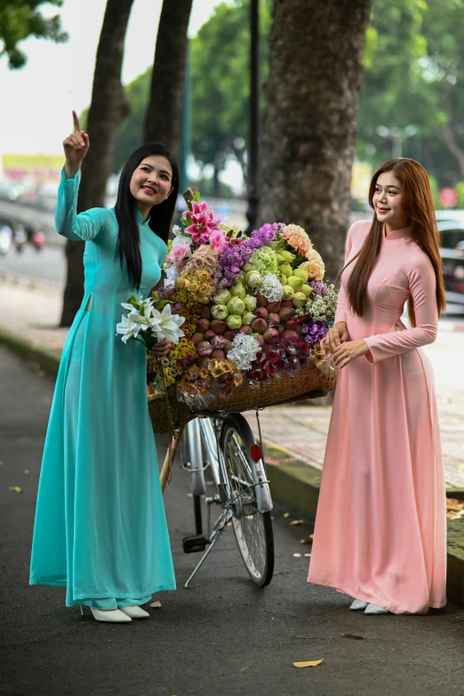 two women stand next to a bicycle and hold a large bunch of flowers