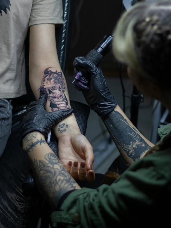 a woman is getting tattooed while another looks on