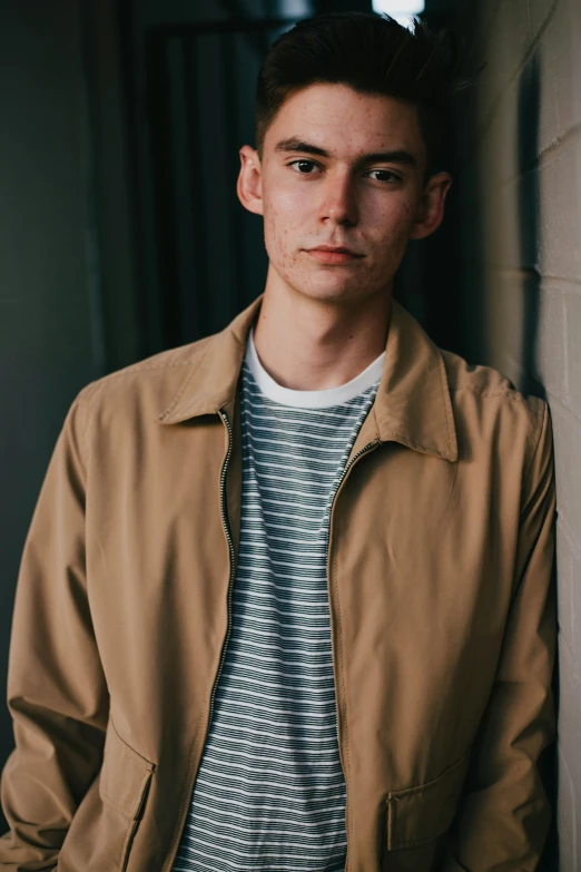 a young man in a jacket leans against a wall