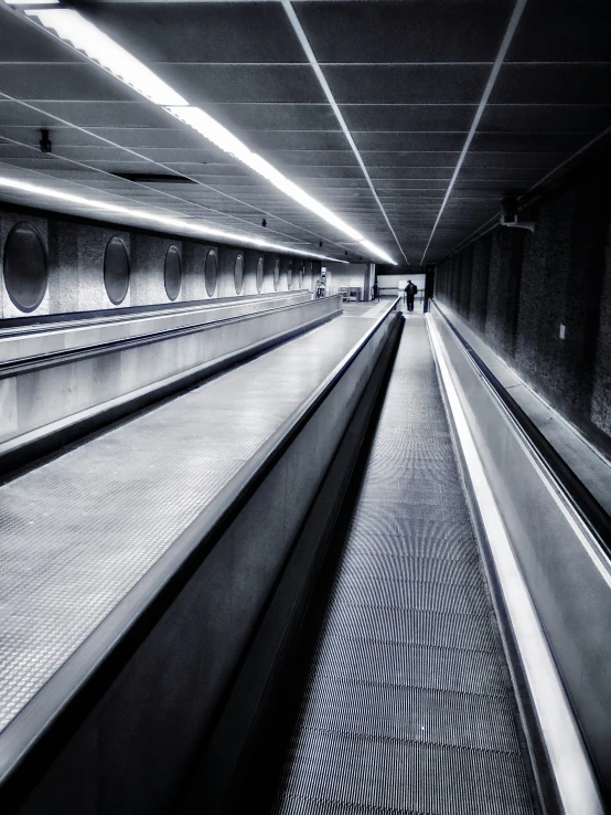 black and white image of an escalator in an underground area