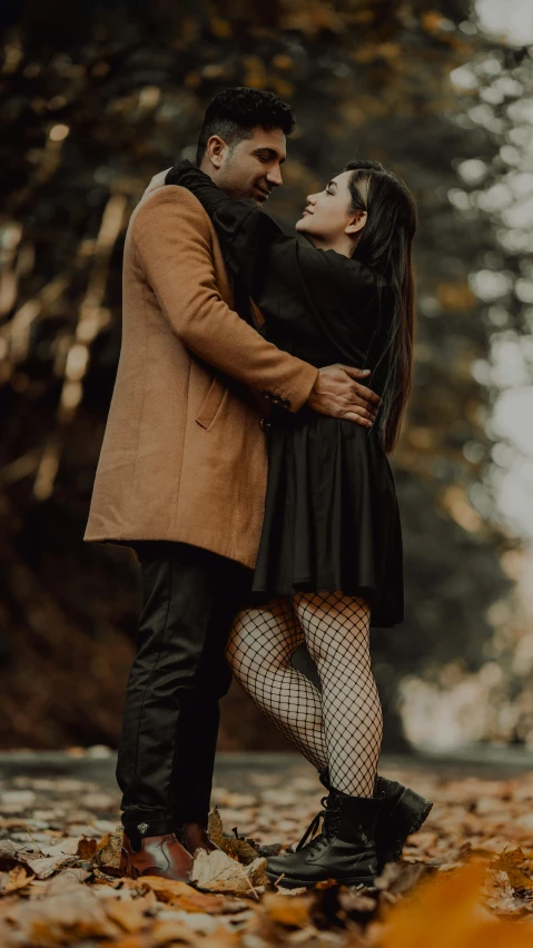 a couple stands together as they stand on leaves in the fall