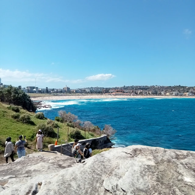 people are standing on the rocks of a cliff overlooking a large body of water