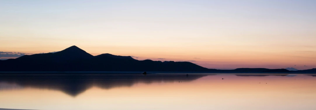 the silhouettes of some mountains and a person is on a lake