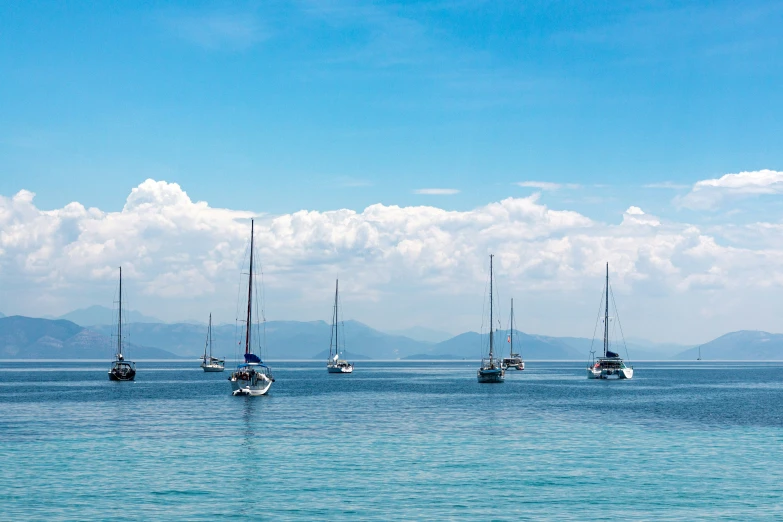 five sailboats sitting in the sea with mountains in the background