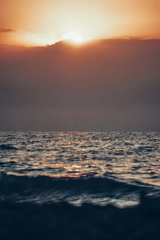 the sun is setting over the ocean with a wave