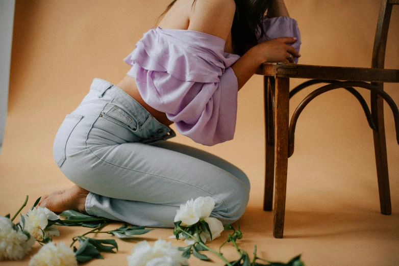 a girl in jeans kneels on the floor with her legs up against a table