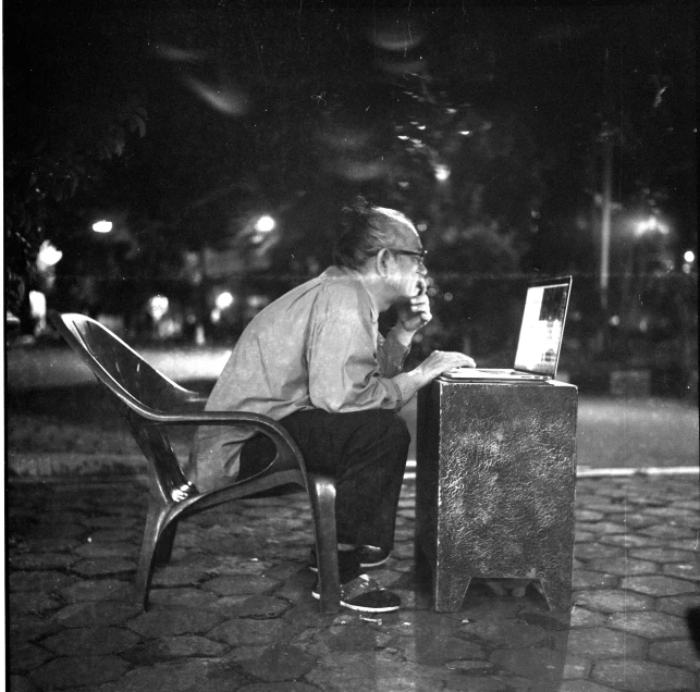 a man is sitting outside at night while working on a laptop