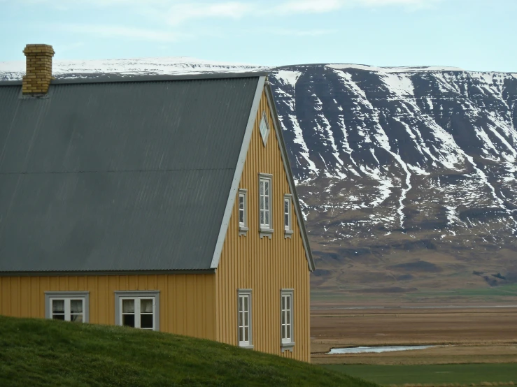 a yellow barn next to a snowy mountain