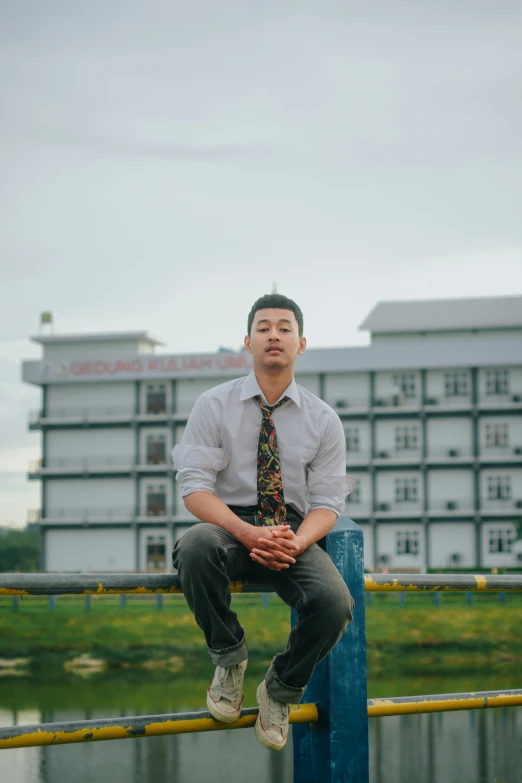 a man in a tie and sneakers sitting on the top of a fence