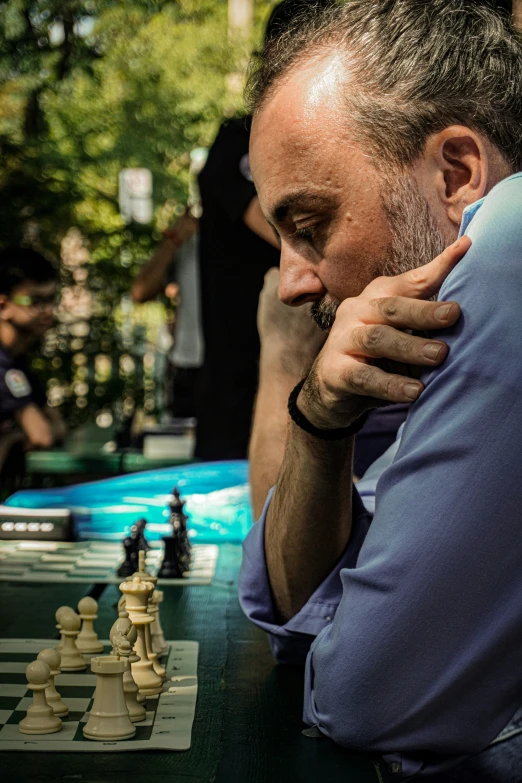 a man holding his head near the chess board while sitting on the bench