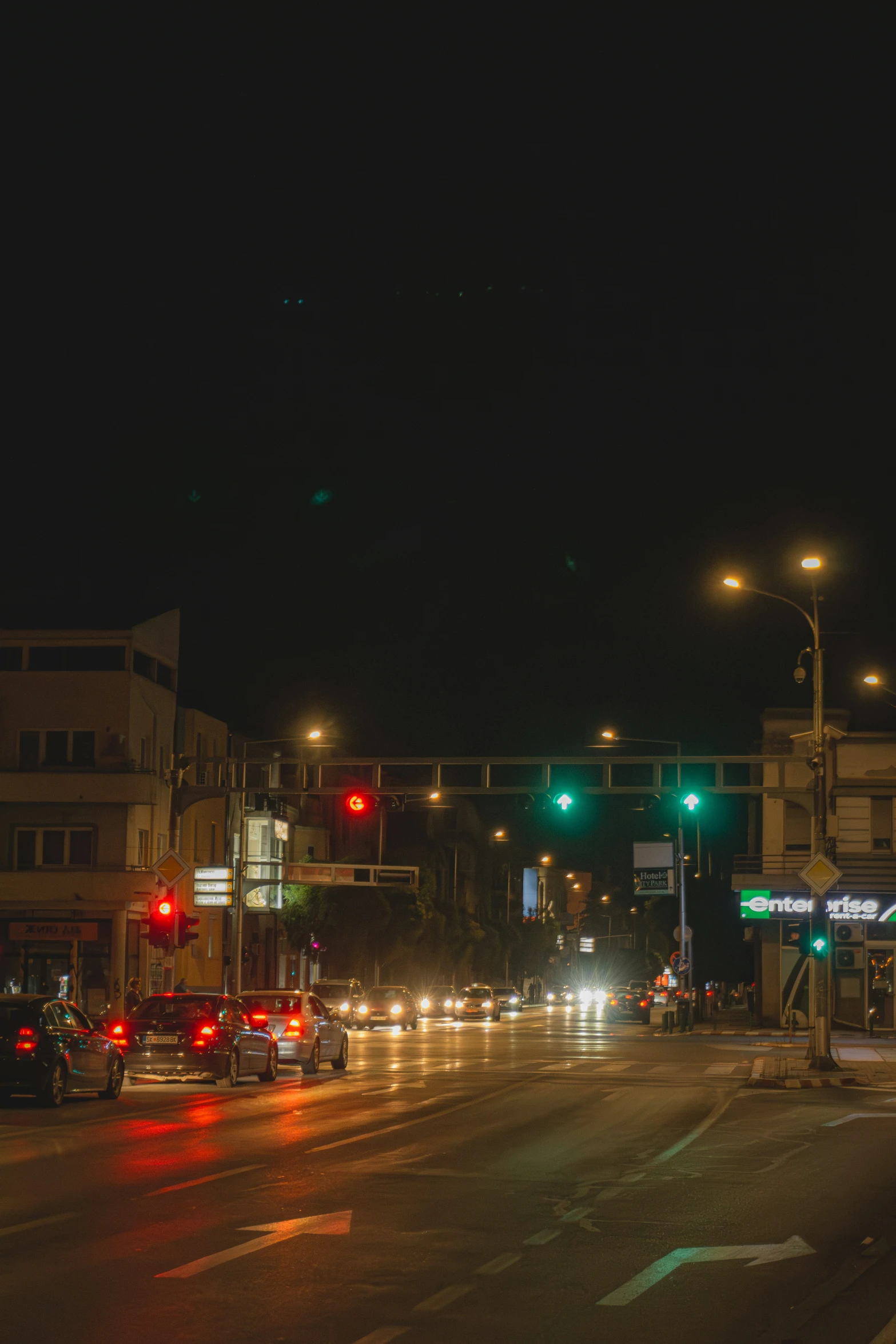 cars driving at night near an intersection under traffic lights