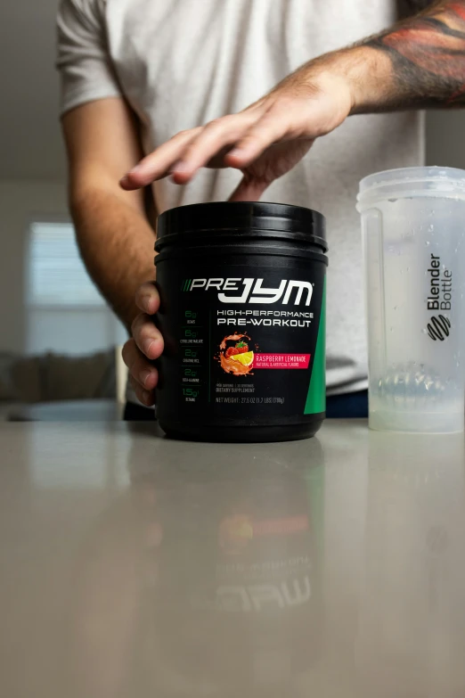 a person with tattoos holding a jar of muscle complex powder