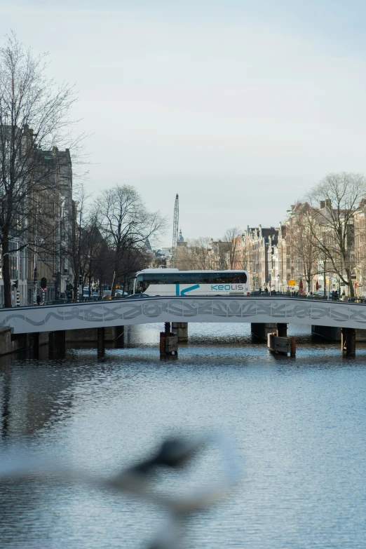 a long white passenger bus traveling on a river next to a bridge