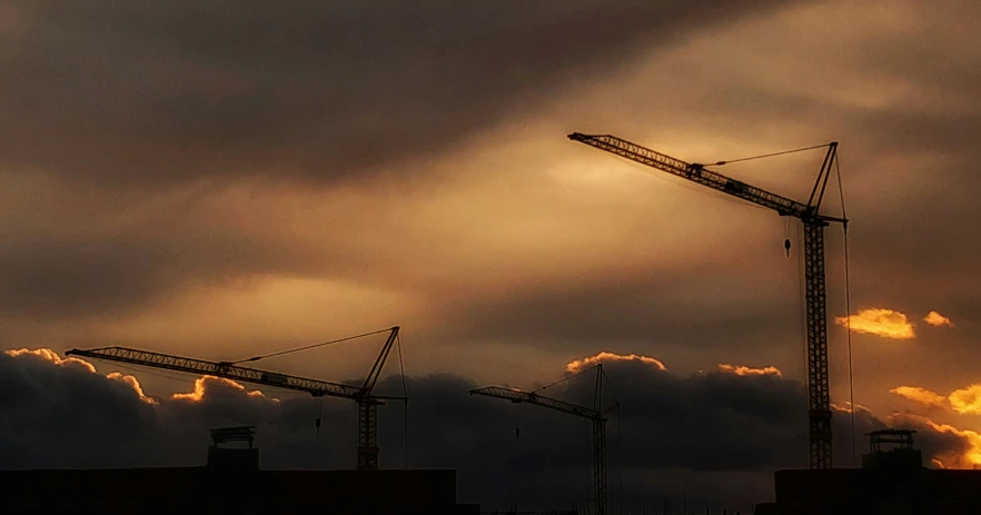 construction cranes silhouetted against a partly cloudy sky