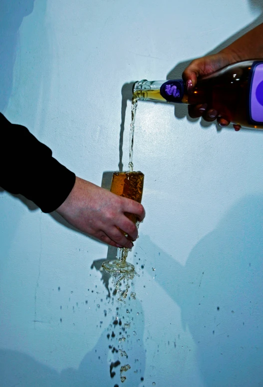 two people with their hands pouring out a bottle of booze