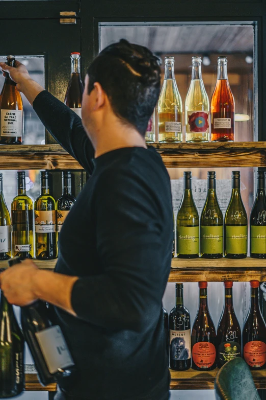 a man in a black shirt putting some wine in the shelf