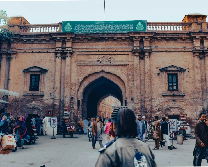 people walking near an old brick building, with an open arch above them