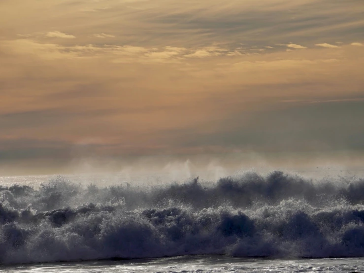 surfers riding waves at sunset with white spray coming from the ocean