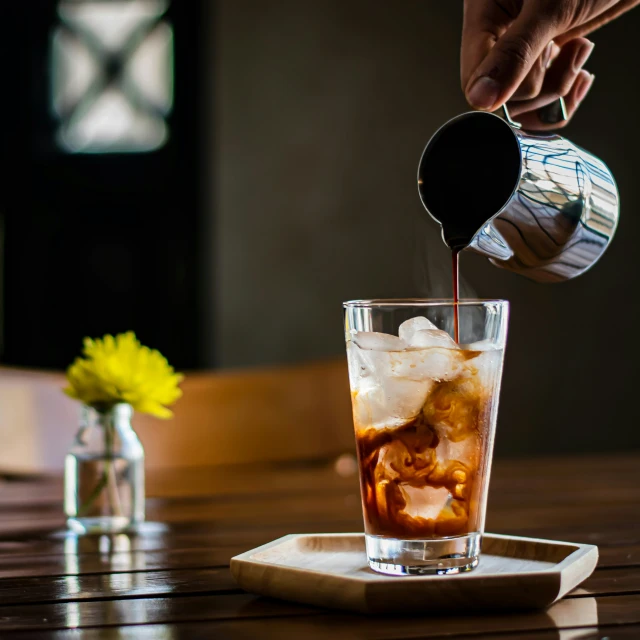 a bartender pours red liquid from a pitcher into the tall glass with ice