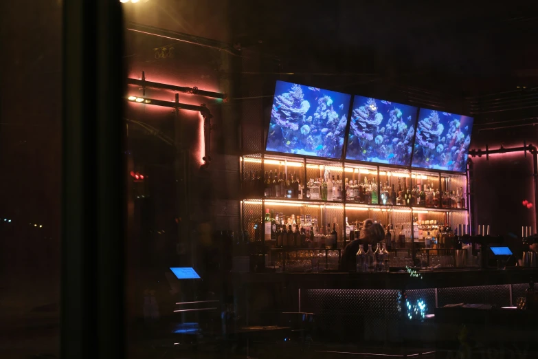 an illuminated bar is shown at night with lots of tv screens