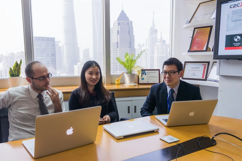 three people are sitting at a table with laptops