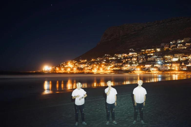 three men standing in the sand at the beach looking into the ocean