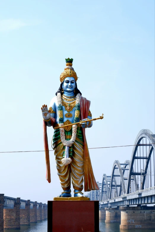 a statue of lord rama standing on a block and overlooking a large bridge
