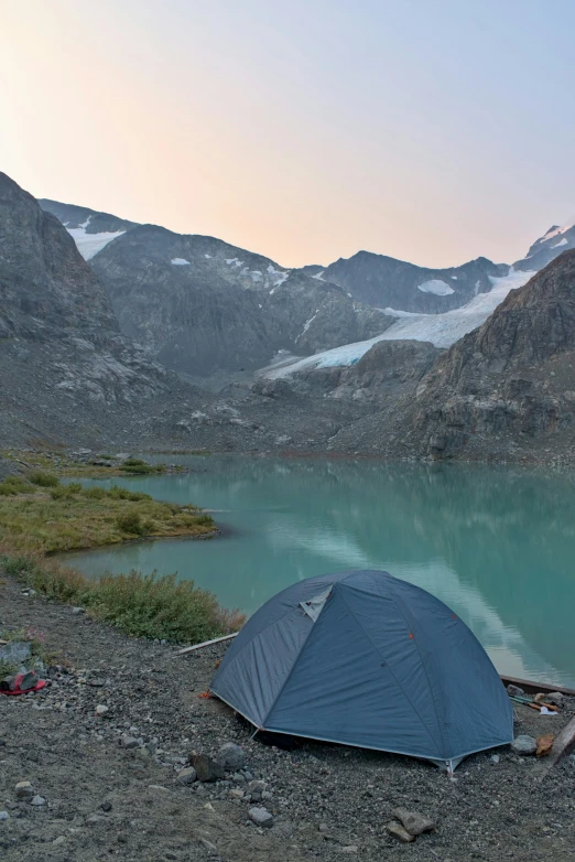 a tent is near a mountain lake, with snow capped mountains