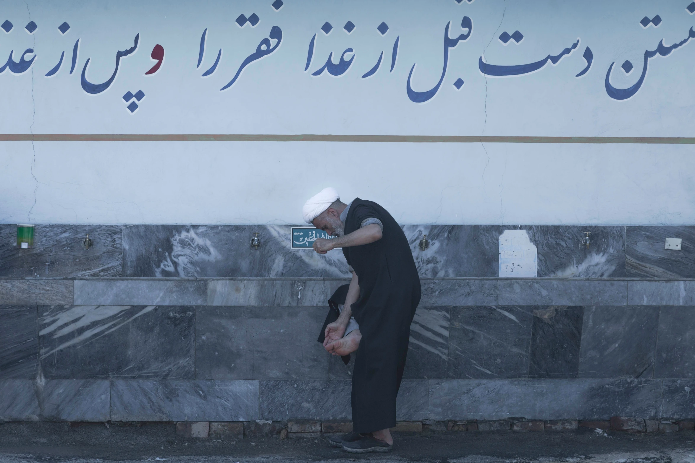 a man in a black dress is leaning against a wall and leaning up against the concrete