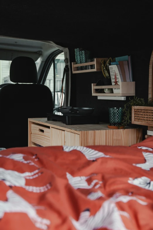 a camper with bed linen, a table and storage unit