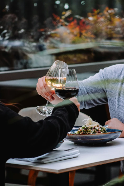 people hold wine glasses in one hand while sitting at an outside table