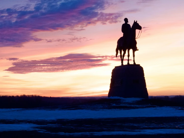 a statue of a man riding a horse under a colorful sky