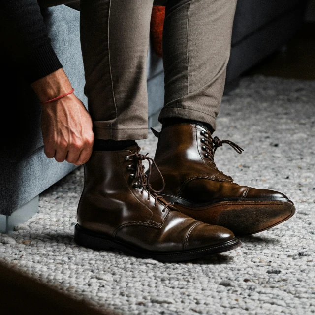 someone is tying their brown shoes together on a carpet