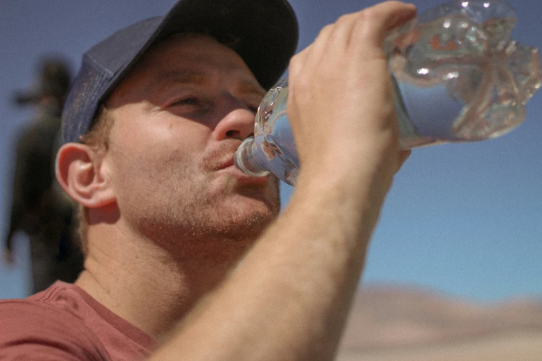 a man with a hat on drinking water from a clear glass