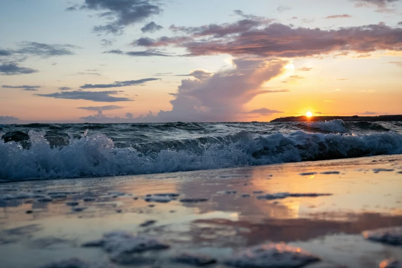 waves are crashing at sunset on the beach